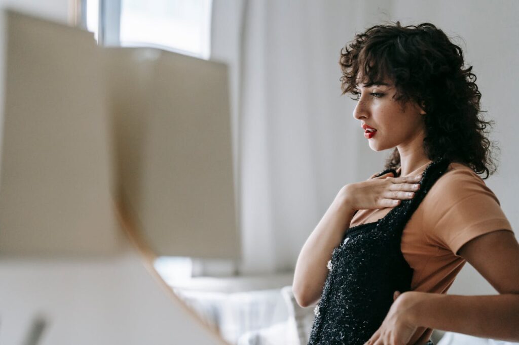 Side view of wistful adult female with black apparel reflecting in mirror and looking away in house